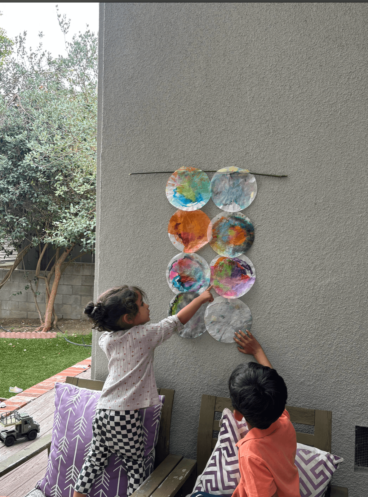 Two kids hanging colorful coffee-filter paintings on an outdoor wall